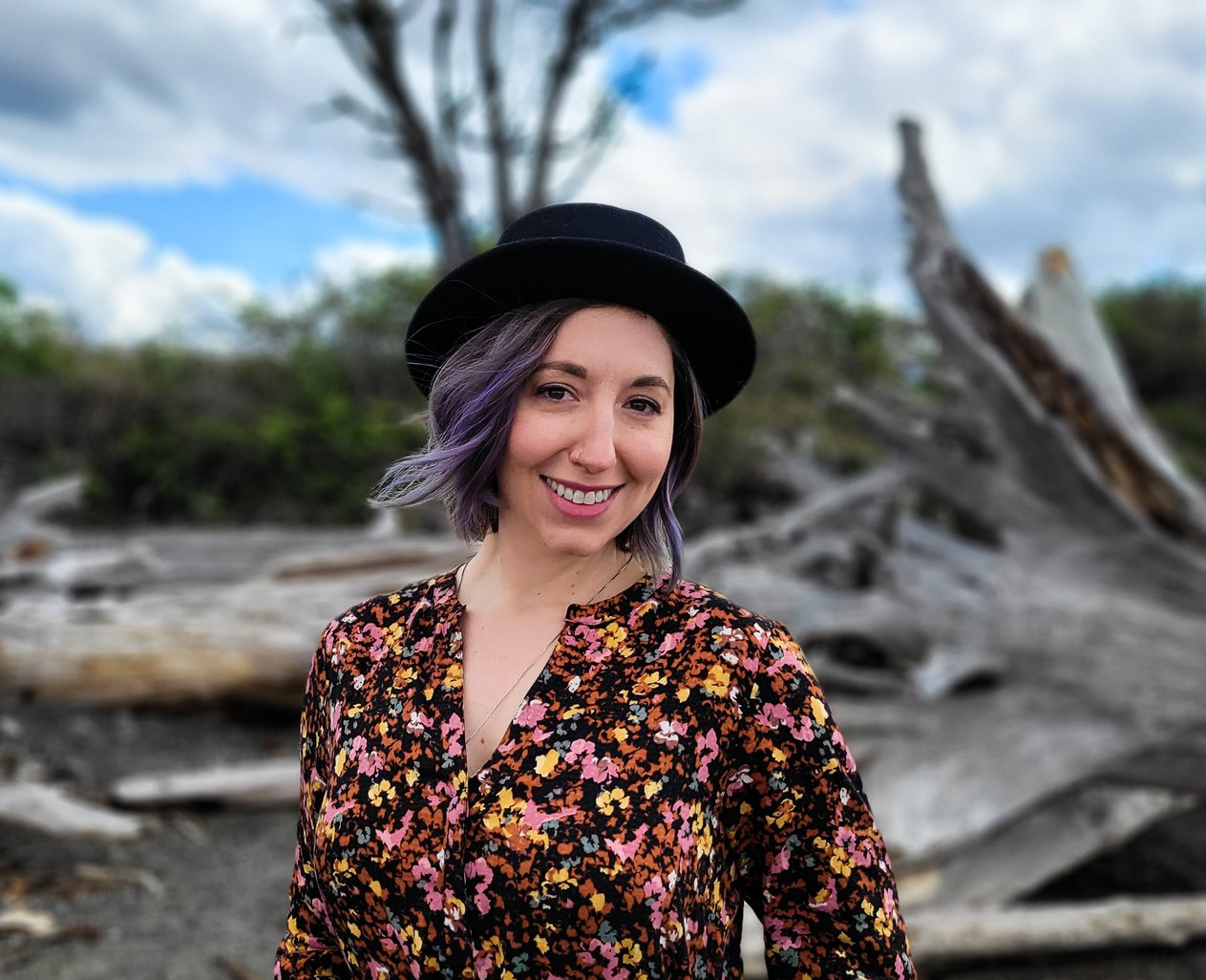 A close-up headshot of Elizabeth Jenkins along the Puget Sound. She is smiling while wearing a floral blouse and black hat.